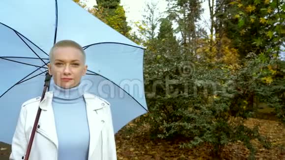 时尚的金发女人带着雨伞在公园散步视频的预览图