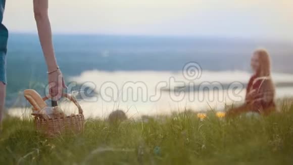 两个可爱的女人坐在田野上野餐一个女人拿着篮子拿着面包和葡萄酒坐着视频的预览图