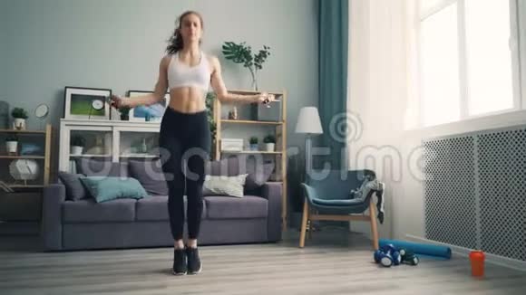 在家里穿着紧身裤和跳绳的瘦女孩集中精力活动视频的预览图