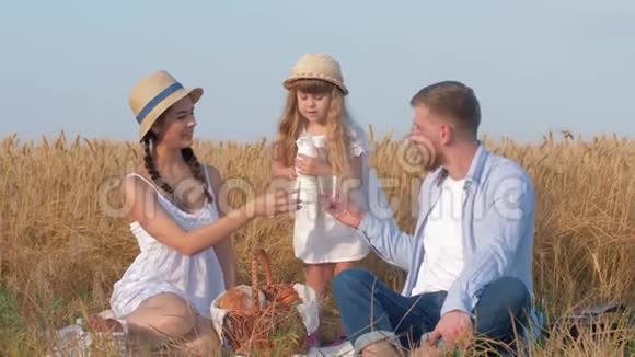 一家人在粮田野餐小女孩在喝牛奶时把牛奶倒进她年轻活泼的父母的眼镜里视频的预览图