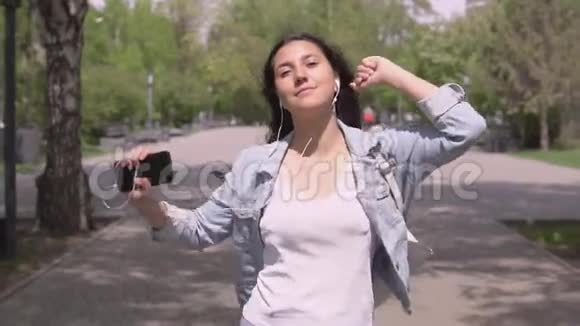 滑稽的长发女孩走在街上用耳机听音乐跳舞视频的预览图