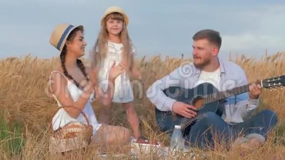 家庭的乐趣年轻开朗的爸爸弹吉他时他美丽的妻子和小女儿高兴地拍手视频的预览图