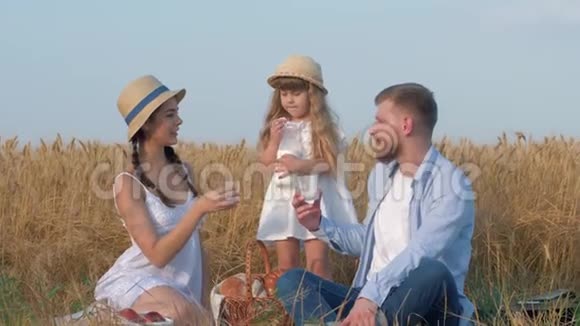 一家人一对年轻幸福的夫妇带着一个可爱的小女孩周末在阳光明媚的庄稼里喝牛奶视频的预览图