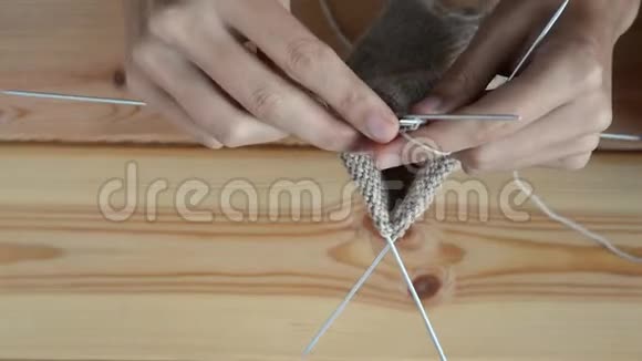 成年女孩在木桌背景上用灰色金属针和羊毛线编织视频的预览图