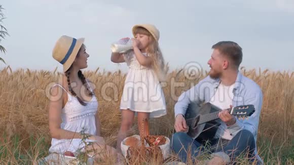 幸福的家庭时刻小可爱的小女孩喝着瓶子里的牛奶而她美丽的父母笑着年轻的爸爸玩着视频的预览图
