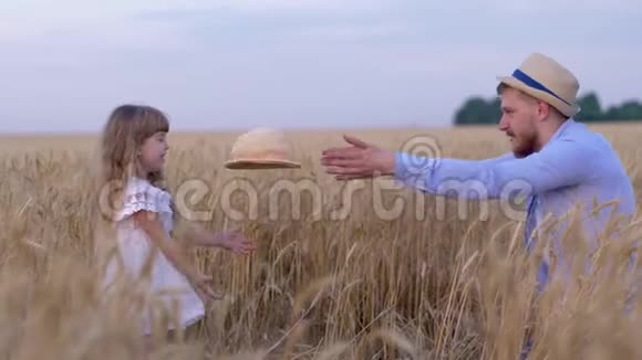 家庭乡村周末年轻英俊的爸爸和他的小女孩一边玩一边用草帽扔东西视频的预览图