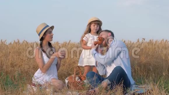 幸福的家庭肖像年轻的父亲从女儿的手中咬着甜面包微笑着坐在露天的女人视频的预览图