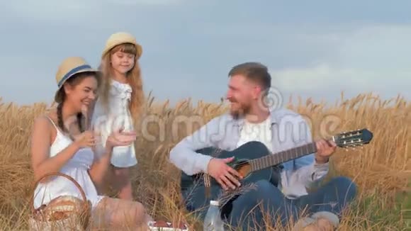 乡间的家庭休闲年轻人弹吉他而他美丽的妻子和小女儿在野餐时欢笑视频的预览图