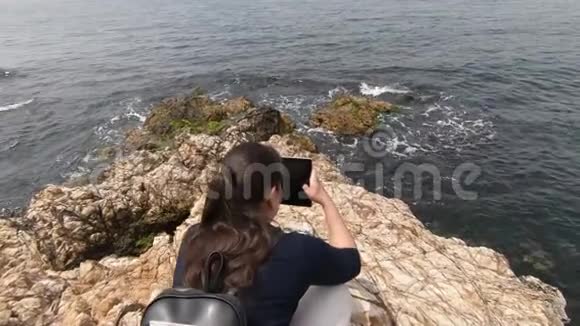 女孩拍了一段录像讲述了海浪在海滩上的岩石上拍得多么漂亮视频的预览图