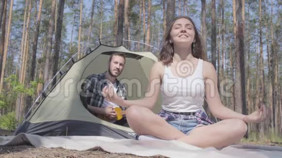 那个年轻的女人在前面打坐而那个男人在后面玩四弦琴坐在帐篷里爱视频的预览图