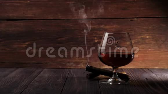 豪华白兰地桌上摆着一杯金色干邑烟从木制桌子上的雪茄中扩散到木制背景上视频的预览图