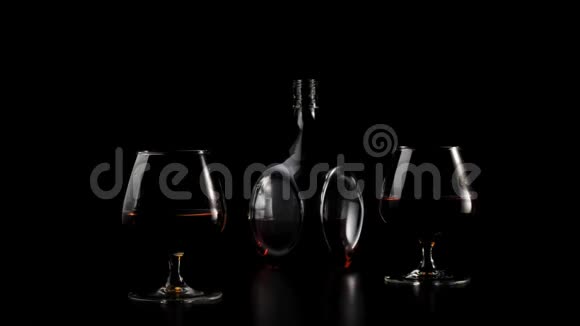豪华白兰地一个圆形瓶子里的金白兰地站在黑色桌子上的两个玻璃杯旁边背景是黑色的光线充足视频的预览图