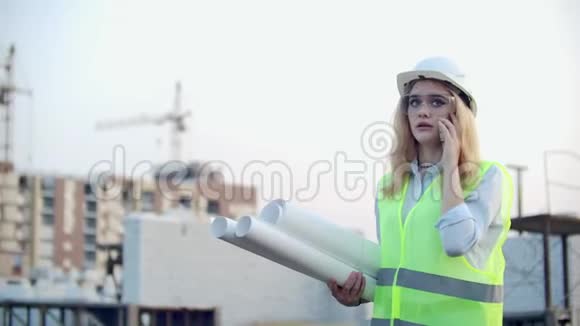 女建筑工人在电话中与承包商交谈他手中拿着图纸在下面的建筑物的背景视频的预览图