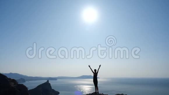 年轻的有灵感的旅行者举起双手站在海面上一座山的顶端映衬着美丽的蓝天视频的预览图