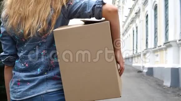 妇女背着一个纸板箱走在室外的后景视频的预览图