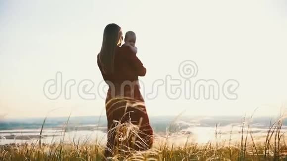 一个女人把一个孩子抱在怀里在日落的背景下视频的预览图