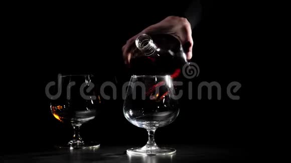 豪华白兰地一个穿着黑色衬衫的人从一个圆形的瓶子里把金色的干邑倒进前景的玻璃杯里白兰地白兰地嗅探器视频的预览图