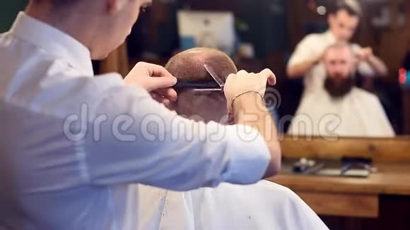男士理发店用剪刀剪发弯着腰的男客户坐在后面镜面反射模糊视频的预览图