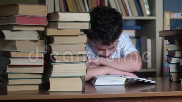 男孩坐在一张木桌旁读一本厚厚的书视频的预览图
