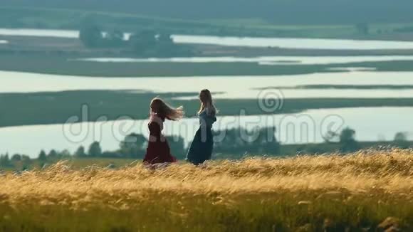 两个女人在湖的背景下在夏天的田野里跳舞和欢笑视频的预览图