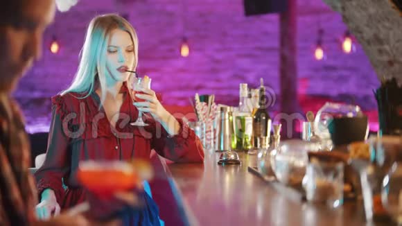 一位漂亮的金发女郎坐在酒保的旁边喝着吸管中的饮料一个男人坐在他的椅子上视频的预览图