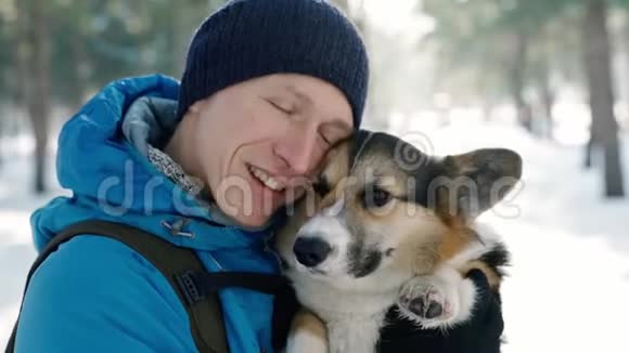温暖的冬衣中快乐的人的情感肖像在寒冷的阳光下在白雪皑皑的冬公园拥抱他的宠物视频的预览图