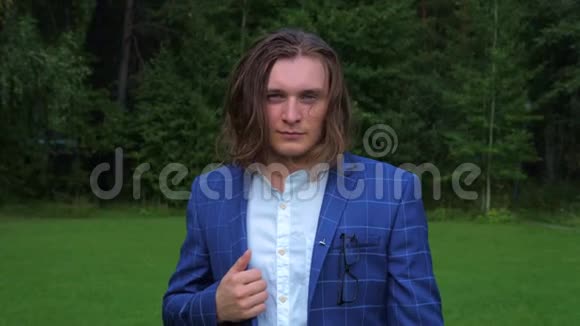 公园里一个长头发身穿商务服的英俊青年的肖像视频的预览图