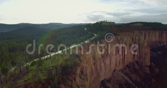 空中视频像一辆白色的拖车沿着高速公路在峡谷的黄色悬崖附近的松树之间行驶视频的预览图