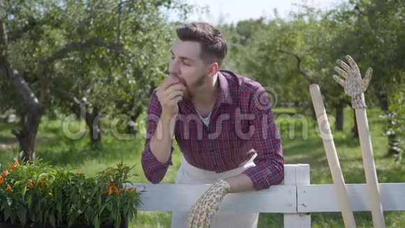 休息的年轻人吃着美味的苹果站在前景夏天的花园在背景那个人在休息视频的预览图