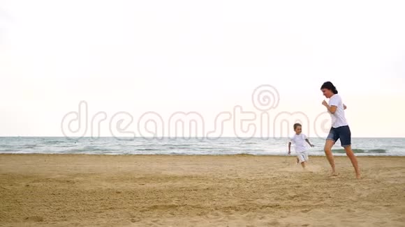 在大海的映衬下一个快乐的男孩和他的妈妈在沙滩上奔跑视频的预览图
