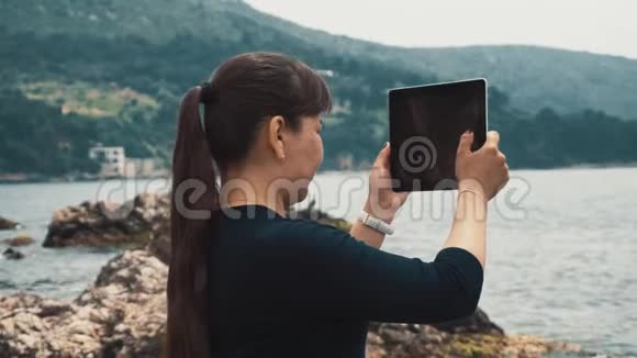 女孩站在一片岩石的海滩上在石碑上拍照美丽的海洋和青山景观视频的预览图