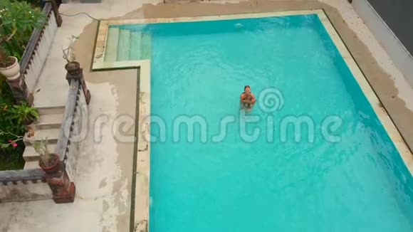 一位年轻女子和她的小儿子在热带游泳池里玩得开心的空中慢镜头视频的预览图