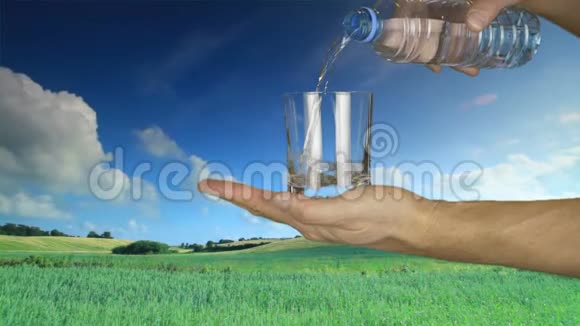 在自然景观背景下人手握玻璃将瓶子中的淡水倒入玻璃中视频的预览图