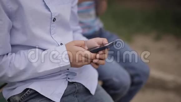 放学后小男孩坐在长凳上玩网络游戏视频的预览图
