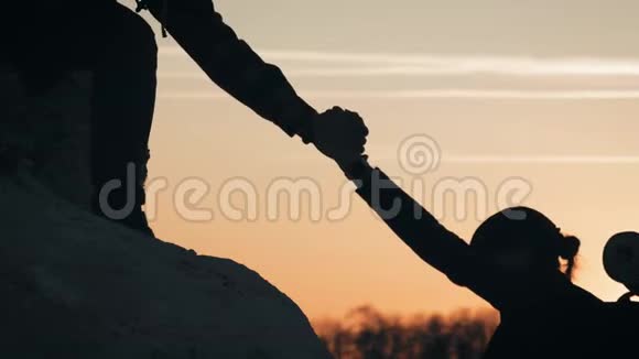 在两个登山者之间帮忙的剪影两个徒步旅行者在山顶上一个男人帮助一个女人攀登一个纯粹的视频的预览图