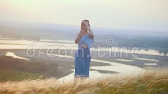 一个金发女人站在田野上在河的背景上自拍视频的预览图
