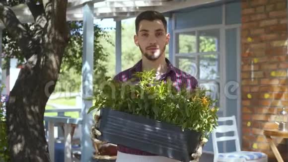年轻微笑的胡子农夫手里拿着一盆花看着镜头微笑地站在前面视频的预览图