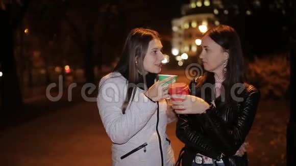 两个女孩晚上在外面被城市的灯点着喝着纸杯里的咖啡说话视频的预览图
