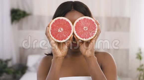 健康的年轻非洲裔美国妇女抱着葡萄柚微笑享受天然护肤美丽视频的预览图