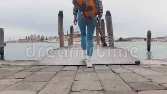 一位年轻女子背着吉他沿着码头走着在河景的尽头视频的预览图