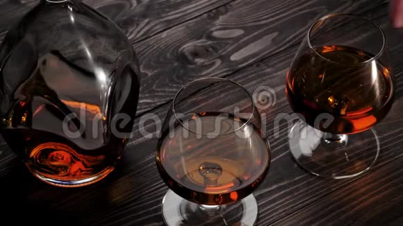 豪华白兰地手从右边从木桌上拿两个玻璃杯中的一个白兰地白兰地嗅探器狂欢慢动作视频的预览图