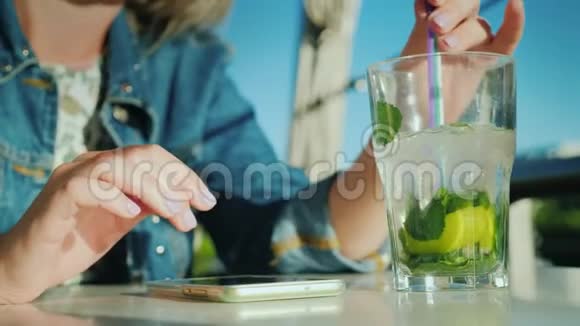 一个女人在咖啡馆里使用智能手机她旁边有一个玻璃杯里面有一杯鸡尾酒休息和商业观念视频的预览图