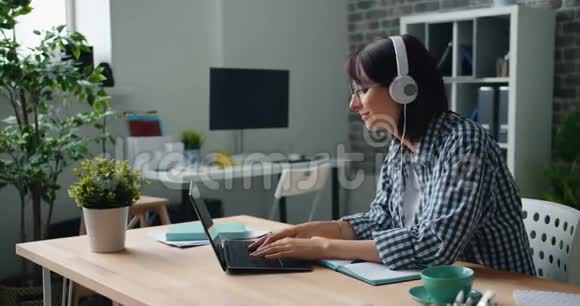 女人在工作中放松听着耳机里的音乐用手提电脑跳舞视频的预览图