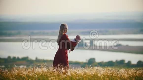 一个穿着红裙子的女人在河的背景下和她的小宝宝在田里玩耍视频的预览图