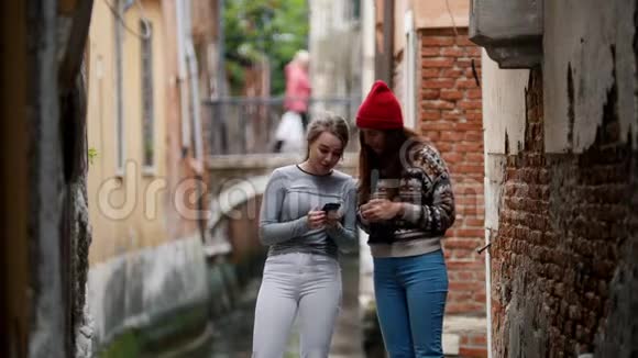 两个年轻迷人的女人站在一个水通道的背景上在电话里听音乐视频的预览图