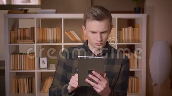 年轻帅气的白人男生在大学图书馆看相机浏览平板电脑特写镜头视频的预览图