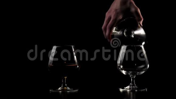 豪华白兰地手把一个圆瓶里的金白兰地倒入黑色桌子上的两个玻璃杯中视频的预览图