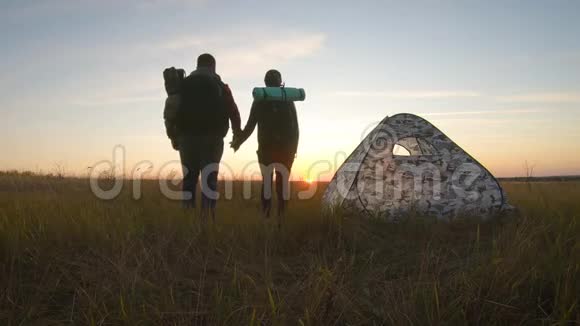 剪影旅游夫妇站在度假帐篷附近手牵手看日落营地休息生活方式视频的预览图