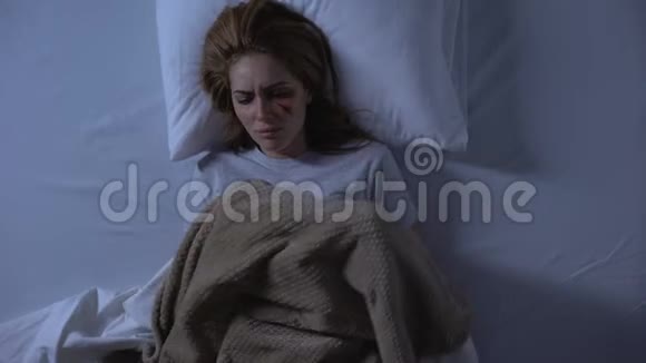 伤心的女人脸上有伤口晚上躺在床上用毯子盖着虐待视频的预览图