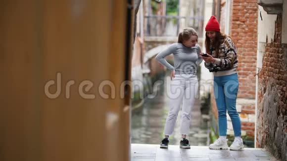两个年轻的笑女站在一条水道的背景上看着电话视频的预览图